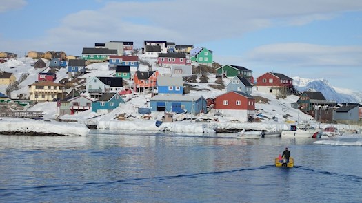 En båd der sejler over spejlblankt vand ind i havn til en by med farverige huse. Det symbolisere hvor tilskuddet bliver brugt i samfundet