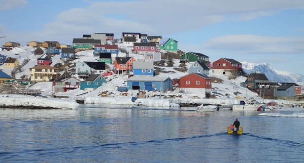 En båd der sejler over spejlblankt vand ind i havn til en by med farverige huse. Det symbolisere hvor tilskuddet bliver brugt i samfundet