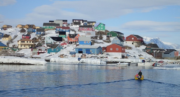 En båd der sejler over spejlblankt vand ind i havn til en by med farverige huse. Det symbolisere hvor tilskuddet bliver brugt i samfundet